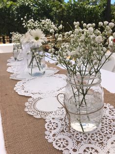 white flowers are in mason jars with lace doily on a table cloth at an outdoor wedding