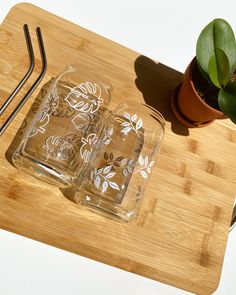 two glasses sitting on top of a cutting board next to a potted plant