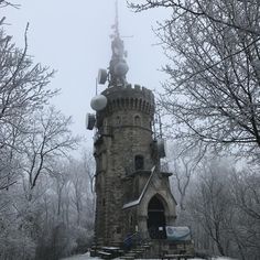 a tall tower with a clock on it's side surrounded by trees and snow