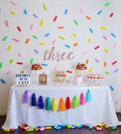 a table topped with cake and cupcakes next to a wall covered in confetti