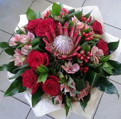 a bouquet of red roses and other flowers on a tile floor with green leaves around it