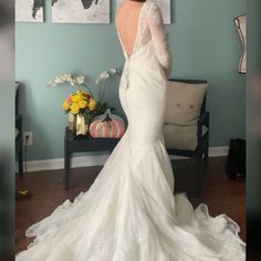 a woman in a white wedding dress is standing near a couch and looking at pictures on the wall