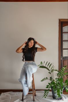 a woman sitting on top of a stool next to a plant