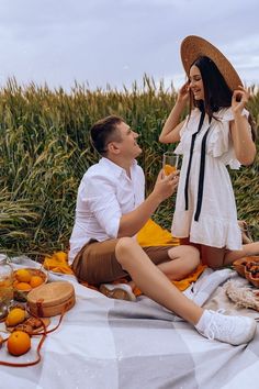 a man and woman sitting on a blanket in front of an orange field with food