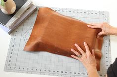 a woman is making a leather pillow on a cutting board