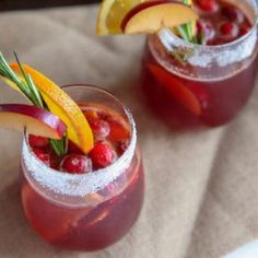 two glasses filled with fruit and garnish on top of a cloth covered table