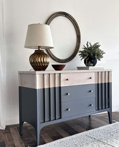 a white and blue dresser with a mirror on top of it next to a lamp