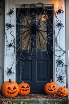 three pumpkins sitting in front of a door decorated with spider web and jack - o'- lanterns