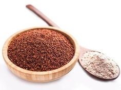 a wooden bowl filled with lots of brown stuff next to a spoon on a white surface