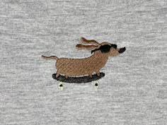 a dog is riding on a skateboard embroidered onto the back of a t - shirt