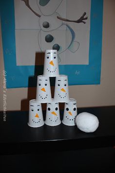 a stack of snowman cups sitting on top of a black table next to a white ball