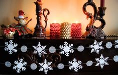 some candles are sitting on a mantle with snowflakes and decorations around it,