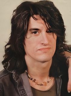 a man with long black hair wearing a leather jacket and holding his hand up to his ear