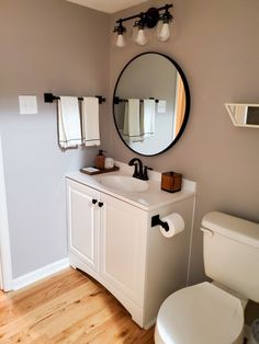 a white toilet sitting next to a bathroom sink under a round mirror on a wall