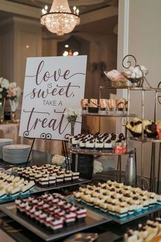 a table filled with lots of desserts and pastries next to a sign that says love is sweet take a treat