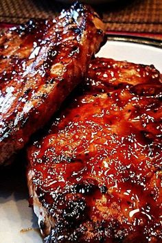 two pieces of meat sitting on top of a white plate covered in bbq sauce