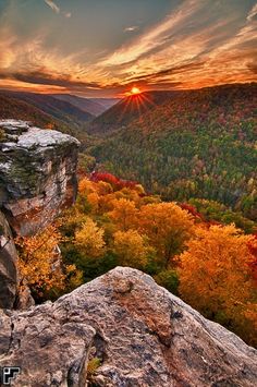 the sun is setting on top of a mountain with trees and rocks in front of it