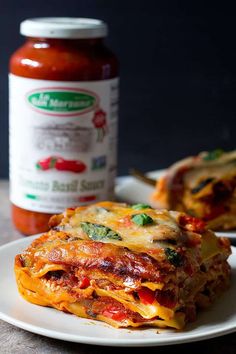 lasagna casserole with tomato sauce and basil leaves on plate next to jar