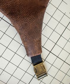 a brown leather seat cushion with a metal buckle on top of white tiled flooring