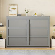 a grey cabinet sitting in the middle of a living room next to a lamp and potted plant