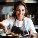 a woman in an apron smiles as she holds a plate with food on it