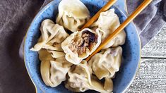 a blue bowl filled with dumplings and chopsticks on top of a wooden table