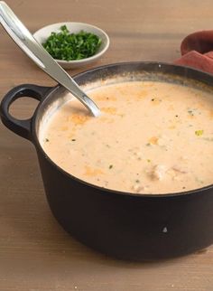 a pot filled with soup sitting on top of a wooden table next to a spoon