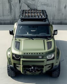 the front end of a green suv parked on top of a cement floor next to a wall