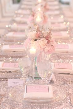 the table is set with pink and white flowers in glass vases, silver napkins, and place cards