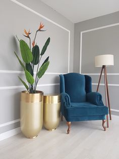 a blue chair sitting next to a gold vase with a plant in it on top of a hard wood floor