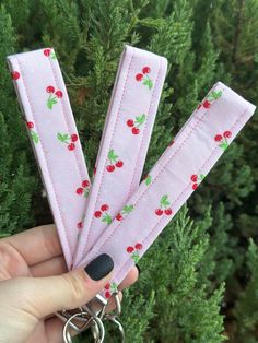 a person holding onto some pink fabric with cherries on it and two silver metal keychains