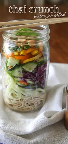 a mason jar filled with noodles and vegetables next to a cup of peanut butter sauce