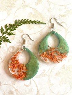 two pairs of green and white earrings with orange glitters on the inside of them