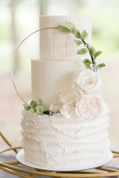 a white wedding cake with flowers and greenery on the top is sitting on a gold platter