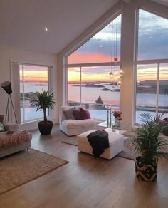 a living room filled with lots of furniture and windows overlooking the water at sunset or dawn