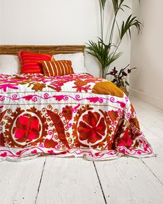 a bed with red and white bedspread on top of it next to a potted plant