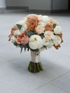 a bridal bouquet with peach and white flowers is on the floor in front of a building