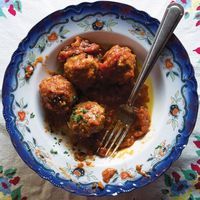 a blue and white bowl filled with meatballs on top of a floral table cloth