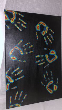 an abstract painting on black paper with multicolored handprints in the middle