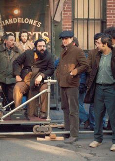 a group of men standing next to each other on a city street near a movie set