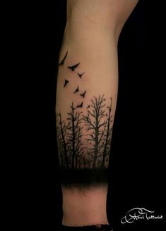 a black and white tattoo with birds flying over trees