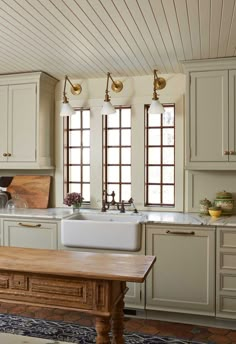 a large kitchen with white cabinets and wooden table in front of the sink, along with two windows