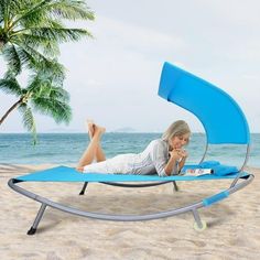 a woman laying on top of a blue chaise lounge chair next to the ocean