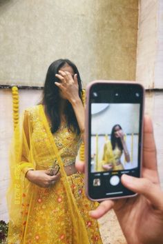 a woman in a yellow sari is taking a selfie with her cell phone