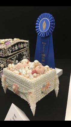 there is a small box with seashells on it next to a blue ribbon