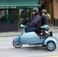 two people riding on the back of a scooter down a street in black and white