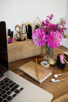 a laptop computer sitting on top of a wooden desk next to a vase filled with flowers