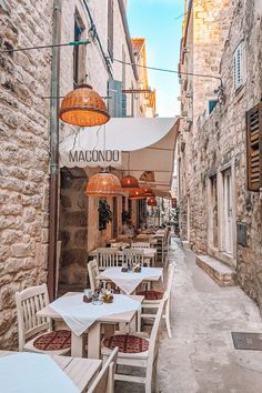 an alleyway with tables, chairs and umbrellas on the sidewalk in front of stone buildings