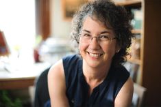 a woman with glasses sitting in front of a bookshelf smiling at the camera