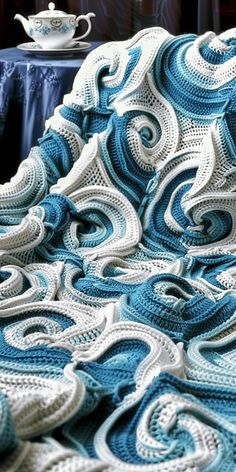 a blue and white crocheted blanket sitting on top of a bed next to a table